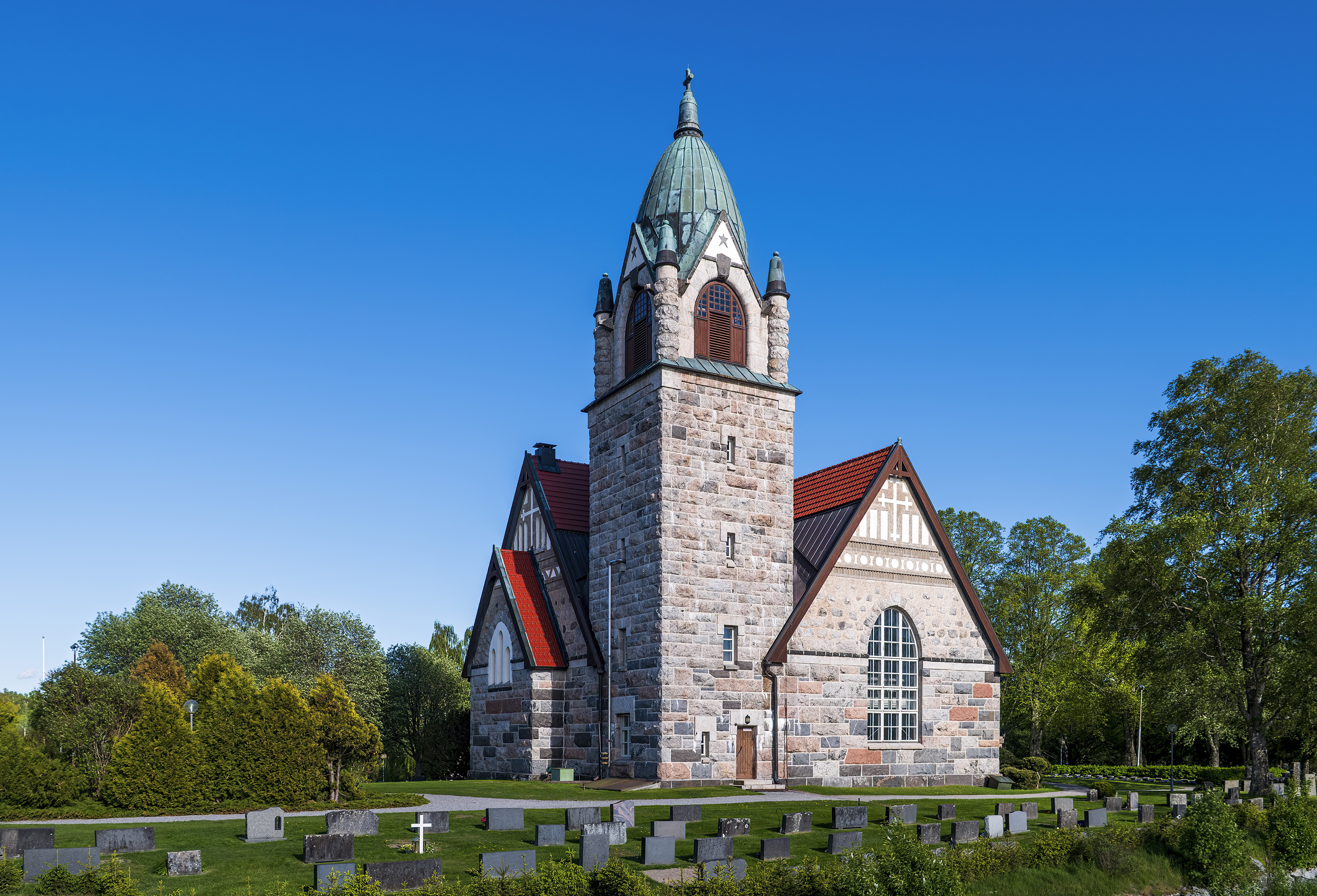 Kivikirkko hautausmaan keskellä ja sininen taivas
